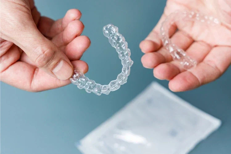 Manos sosteniendo un par de alineadores transparentes