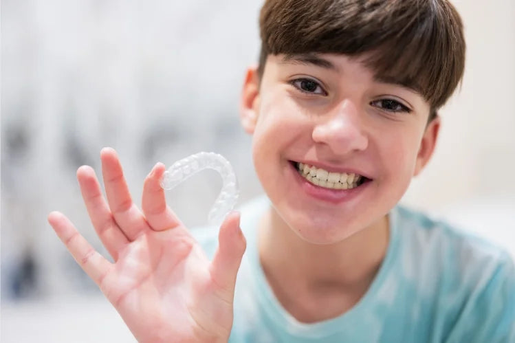 Un adolescente sonriente sosteniendo brackets transparentes